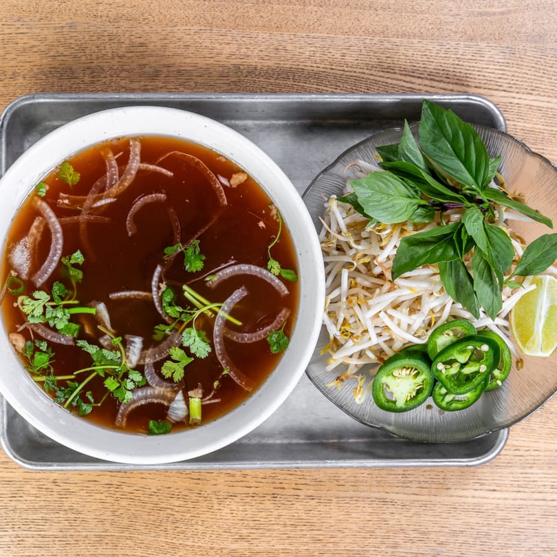 Vietnamese pho with onions and cilantro, served with a side of bean sprouts, basil, jalapeños, and lime.