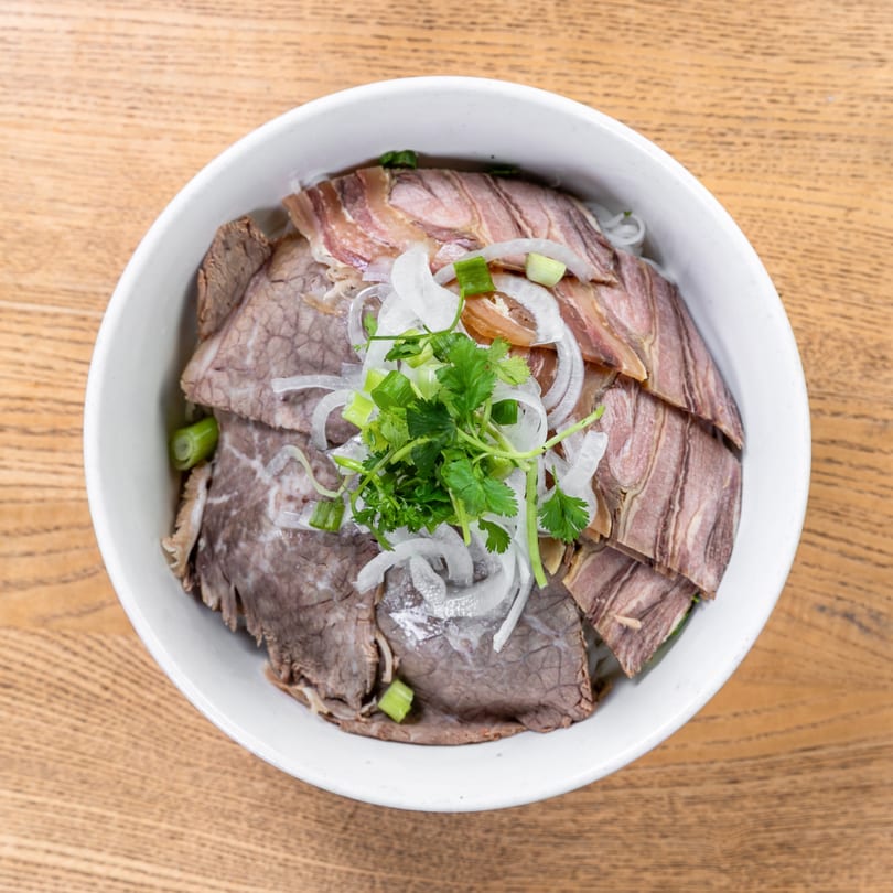 Overhead view of a Vietnamese pho bowl with sliced beef, onions, and cilantro.